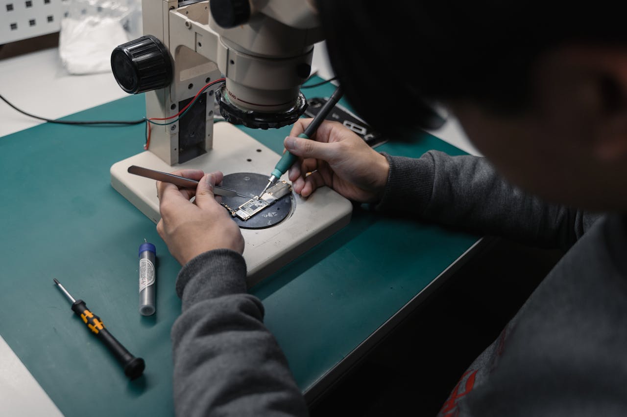services-02 Technician using a microscope to repair a broken electronic board with precision tools.